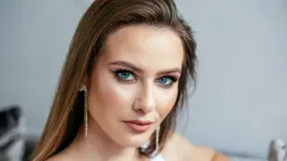 Kobieta z brązowymi włosami i niebieskimi oczami, idealnie dobrany kolor włosów do niebieskich oczu. Długie, błyszczące kolczyki dodają elegancji.