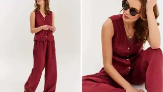 Kobieta w bordowym lnianym komplecie: kamizelka i szerokie spodnie. Stylizacja z okularami przeciwsłonecznymi i naszyjnikiem. Lampas na spodniach dodaje elegancji.