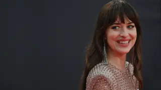 Uśmiechnięta kobieta z burzą brązowych włosów i grzywką w stylu birkin bangs, w błyszczącej sukni i długich kolczykach.