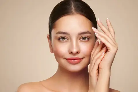 Portret kobiety z gładką cerą i dłońmi delikatnie dotykającymi twarzy.