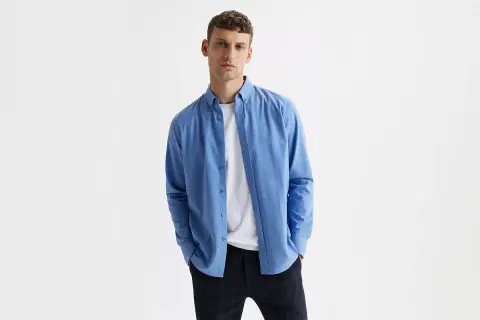 Mężczyzna w niebieskiej koszuli i białej bluzce pod spodem, w kratę spodnie. Idealny zestaw smart casual.