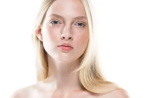 Młoda kobieta o jasnej cerze i blond włosach, uosobienie skandynawskiej urody. Delikatne rysy twarzy, błękitne oczy i subtelny rumieniec.