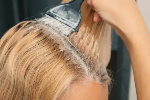 Nakładanie farby na blond włosy, tworząc subtelne refleksy.