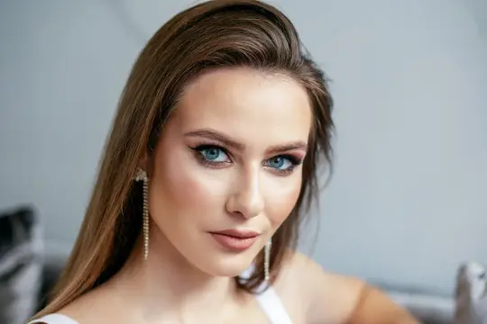 Kobieta z brązowymi włosami i niebieskimi oczami, idealnie dobrany kolor włosów do niebieskich oczu. Długie, błyszczące kolczyki dodają elegancji.