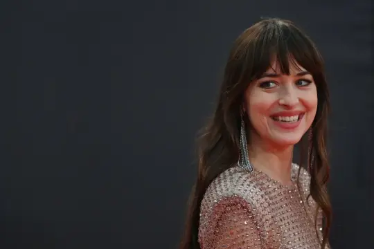 Uśmiechnięta kobieta z burzą brązowych włosów i grzywką w stylu birkin bangs, w błyszczącej sukni i długich kolczykach.