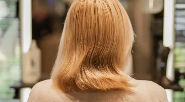 Kobieta z blond włosami, które zaczynają przechodzić w siwe. W tle widać salon fryzjerski.