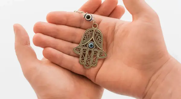 Dłonie trzymają ozdobny amulet ręka Fatimy z niebieskim okiem.