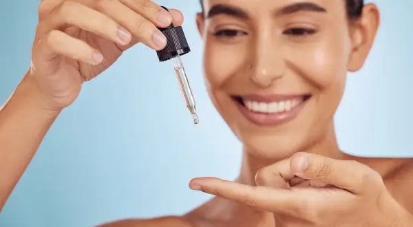 Uśmiechnięta kobieta pokazuje, jak stosować retinol, aplikując kroplę serum na palec.