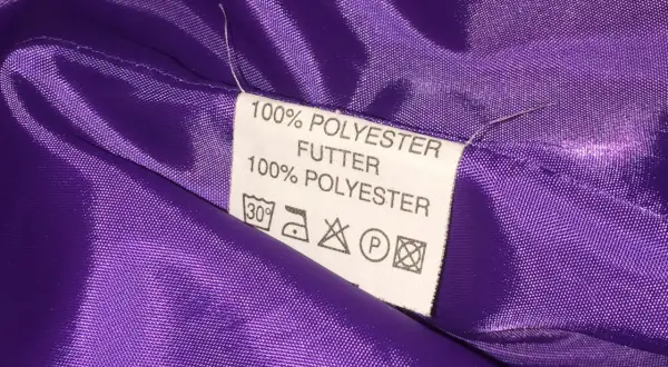 Metka z informacją "100% POLIESTER FUTTER" na fioletowym materiale. Czy poliester jest zdrowy? To pytanie nurtuje wiele osób.